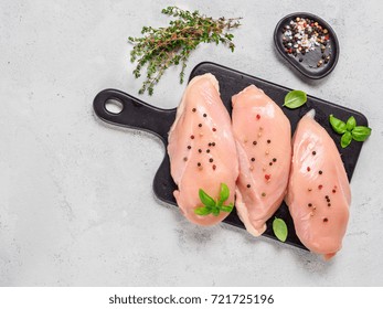 Raw chicken breast with fresh basil and thyme on black cuttingboard. Raw chicken fillet on gray cement background. Copy space. Top view or flat lay.