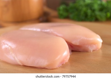 Raw Chicken Breast With Wooden Mortar And Fresh Parsley In The Back (Selective Focus, Focus On The Front Of The Meat)