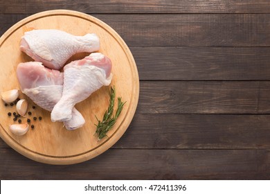 Raw chicken drumsticks on cutting board on wooden background. Copy space for your text.
