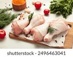 Raw chicken drumsticks with spices on cutting board on light background.