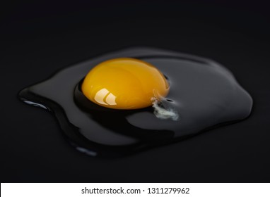 Raw Chicken Egg On A Black Surface. Raw Yolk And Protein Of Chicken Egg On A Black Surface, Side View.