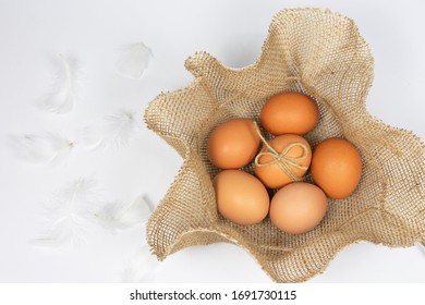 Raw chicken eggs in a straw nest with white feathers. White background and Copy space. Easter concept. Farm products, natural eggs.