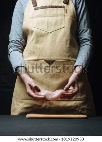 Raw chicken fillet in woman hands on black background.