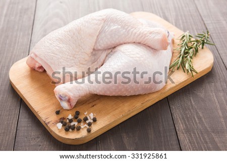Raw chicken leg on cutting board on wood table.