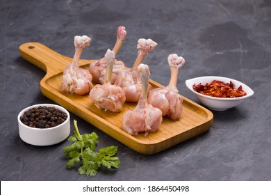 Raw chicken lollipop,six pieces of chicken lollipop arranged on a serving board with black pepper,chilli flakes and coriander leaf with grey textured background