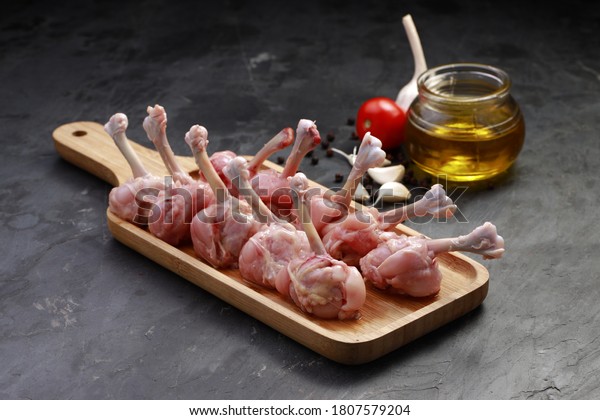 Raw chicken lollipop,ten pieces of chicken\
lollipop arranged on a serving board with oil, tomato and garlic on\
background with grey textured\
base