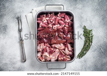 Raw chicken offals meat set, gizzards, stomachs, liver and hearts in a steel tray with herbs. White background. Top view.