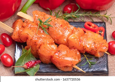 Raw chicken skewers in marinade with spices on a black plate and on a wooden table. Raw marinated and spicy chicken skewers.Top view. Chicken meat close up. Raw meat in marinade. Tasting diet meat.