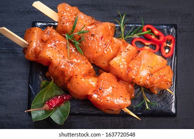 Raw chicken skewers in marinade with spices on a black plate and on a wooden table. Raw marinated and spicy chicken skewers.Top view. Chicken meat close up. Raw meat in marinade. Tasting diet meat.