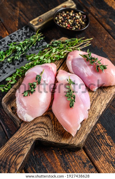 Raw Chicken skinless thigh fillet\
on a wooden cutting board. Black background. Top\
view.
