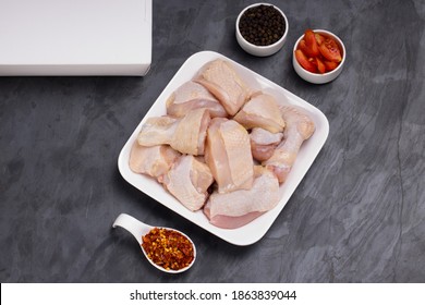 Raw Chicken Tender Curry Cut With Skin Arranged On White Plate And Garnished With Black Pepper And Tomato Slices On  Graphite Colour Background With Take Away Box