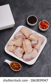 Raw Chicken Tender Curry Cut With Skin Arranged On White Plate And Garnished With Black Pepper And Tomato Slices On  Graphite Colour Background With Take Away Box