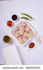 Raw Chicken Tender Curry Cut With Skin Arranged On White Plate And Garnished With Garlic ,black Pepper,green Chilli,tomato Slices,oil And Chilli Flakes On White Background With Take Away Box