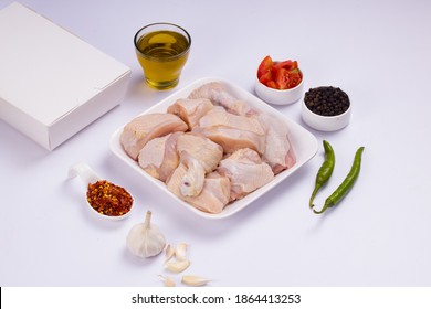 Raw Chicken Tender Curry Cut With Skin Arranged On White Plate And Garnished With Garlic ,black Pepper,green Chilli,tomato Slices,oil And Chilli Flakes On White Background With Take Away Box