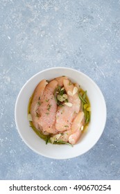 Raw Chicken Tenders Marinated With Garlic, Olive Oil, Lemon Juice, Rosemary, Thyme, Salt And Pepper In White Bowl