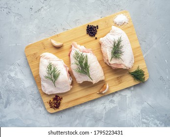 Raw chicken thighs on cutting board with ingredients for cooking at grey concrete kitchen table. Top view with copy space.