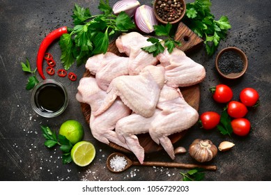 Raw chicken wings with ingredients for cooking on a wooden cutting board over dark slate or metal background.Top view . - Shutterstock ID 1056729203