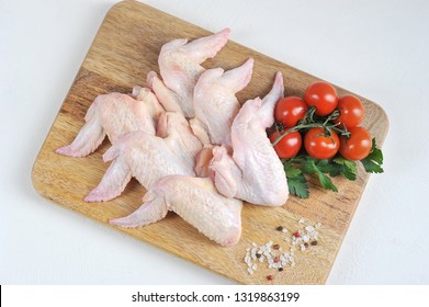 Raw Chicken Wings On A Wooden Board. The Composition Is Complemented By Cherry Tomatoes, Parsley And Spices. White Background. Close-up. View From Above.