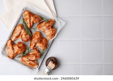 Raw chicken wings, rosemary, marinade and basting brush on light tiled table, flat lay. Space for text - Powered by Shutterstock