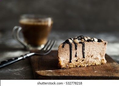 Raw Chocolate Mousse Cake  With Cashew Nuts, Hazelnuts And Dark Chocolate Glaze Topping And Coffee On A Wooden And Grey Stone Background. Vegan Sugar, Gluten, Dairy Free Dessert. Horizontal