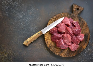 Raw chopped beef on a wooden cutting board on a slate,stone or concrete background.Top view.