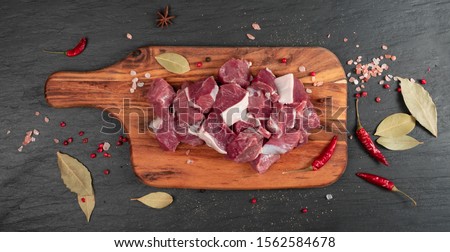 Raw chopped lamb fillet, diced tenderloin or cubed mutton sirloin meat on black stone plate background. Fresh sheep fillet, loin filet with spices on wood board top view