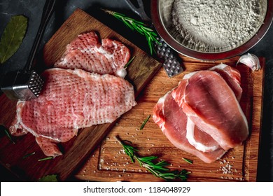 Raw chops and pieces of pork for escalopes on cutting boards with flour, rosemary, bay leaf, garlic, hammer and sauce on the kitchen table. Top view, closeup
