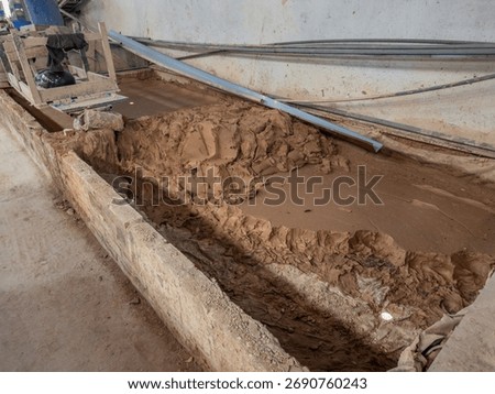 Raw clay slurry in an industrial processing trench, indicating the initial stages of material preparation for manufacturing. This factory interior shows raw materials in an unfinished, gritty state,