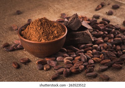 Raw cocoa beans, clay bowl  with cocoa powder, chocolate on sacking