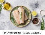 Raw cod fillet on ceramic plate with aromatic herbs, lime, salt and olive oil on gray background. Healthy seafood. top view