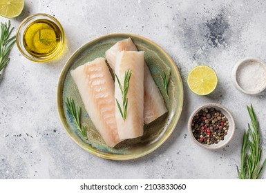 Raw cod fillet on ceramic plate with aromatic herbs, lime, salt and olive oil on gray background. Healthy seafood. top view