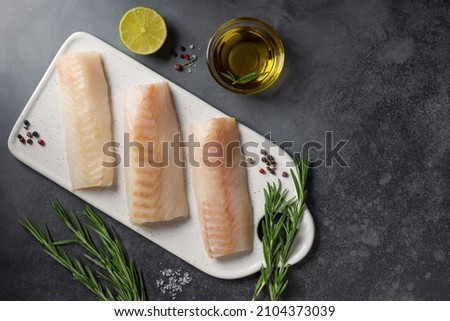 Raw cod loin fillet steak with ingredients for cooking on cutting board. Mediterranean cuisine. dark background with copy space
