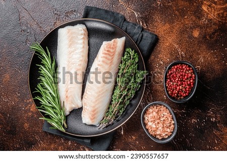 Raw cod loin fillet steaks with herbs on plate. Dark background. Top view.