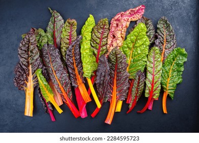 Raw colourful chard offered as a close-up on a rustic black board 