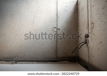 Raw concrete wall with exposed electrical cable and recessed conduit channel during unfinished building construction and renovation.