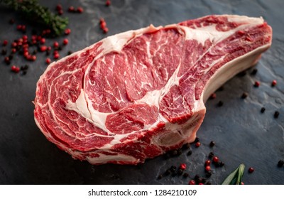 raw cowboy steak with seasonings on stone background, prime rib eye on bone