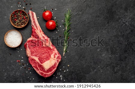 Raw cowboy steak with spices on stone background