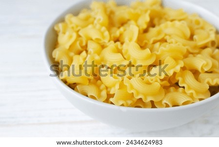 Raw Creste Di Gallo pasta in a gray bowl on a white wooden board. Rooster comb. The concept of traditional Italian food. Horizontal orientation. Copy space. Selective focus