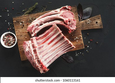 Raw cut rack of lamb. Fresh meat on wooden board at black background. Organic ingredients for restaurant meals , top view, copy space
