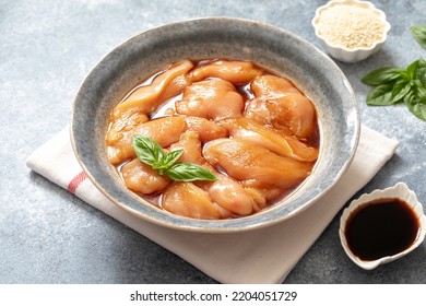 Raw diet marinated chicken meat with teriyaki sauce in a grey bowl. Marinating meat for cooking barbecue