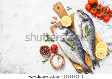 Raw dorado fish on cutting board on white table with ingredients for cooking. Top view with copy space.