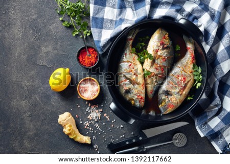 Raw dorado fishies marinated with spices, sea salt, ginger, soy sauce and herbs in a baking dish on a concrete table with ingredients, view from above, flatlay