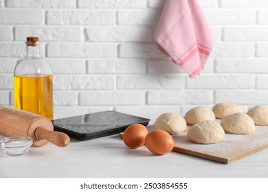 Raw dough balls, eggs, oil, rolling pin and kitchen scale on white wooden table - Powered by Shutterstock