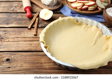 Raw dough and ingredients on wooden table, space for text. Baking apple pie