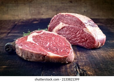 Raw Dry Agd Angus Rib-eye Beef Steak Offered As Close-up On A Rustic Burnt Wooden Board