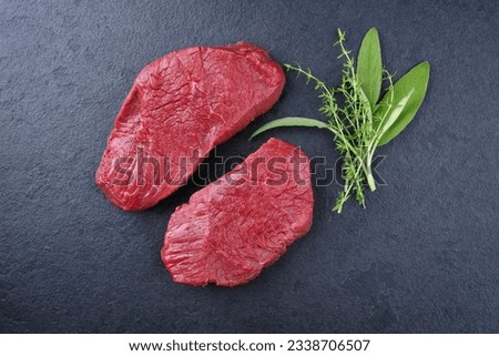 Raw dry aged bison beef rump steak slices with herbs offered as top view on black background with copy space 
