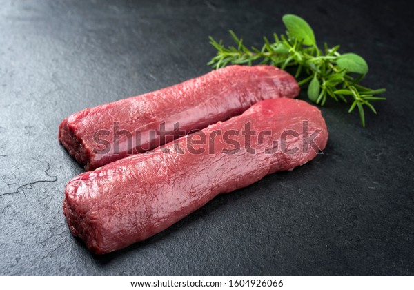 Raw dry aged venison\
tenderloin fillet steak natural with herbs offered as closeup on a\
modern design board 