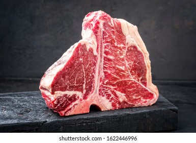 Raw dry aged wagyu porterhouse beef steak with large fillet piece as closeup on a black burnt wooden board with copy space