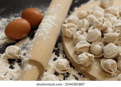 Raw dumplings, selective focus. Cooking pelmeni, flour, eggs and wooden rolling pin. Meat pelmeni or ravioli on wooden board, dark table. Slavic traditional dish. Food background - Powered by Shutterstock