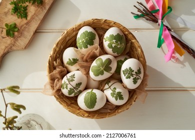 Raw Easter eggs with herbs attached to them in a basket, ready to be dyed with onion peels, top view